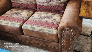 A Galaxy S22 Ultra on a brown leather sofa with patterned cushions, a wooden side table, and a carpeted floor.