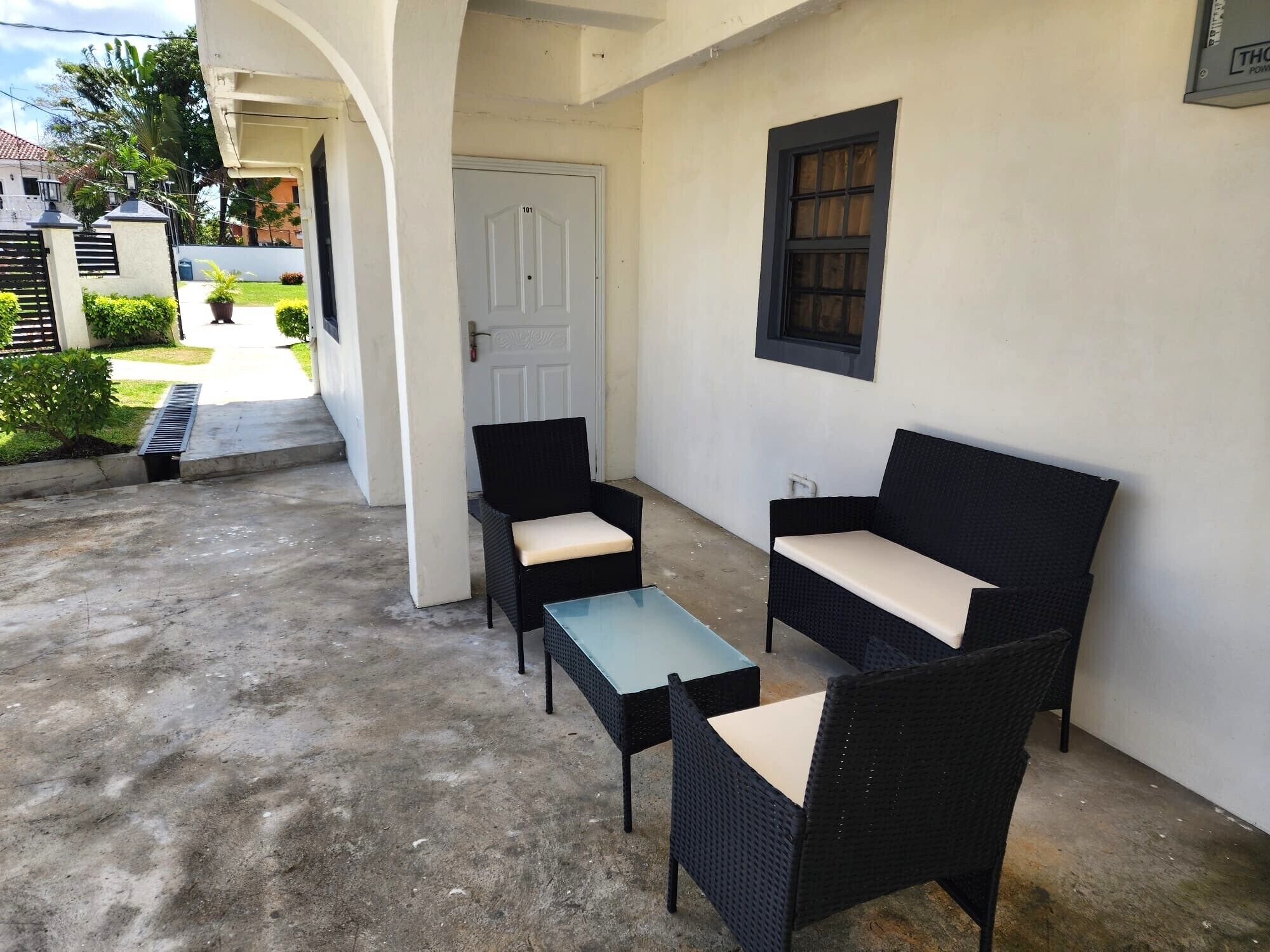 A patio area with two black wicker chairs and a small table, a white door, and a window with a dark frame.