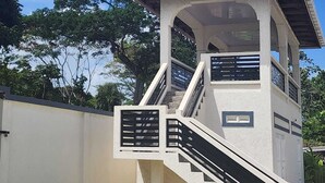 Un escalier extérieur abrité mène à une construction au toit rouge, à la façade blanche et aux rampes noires.