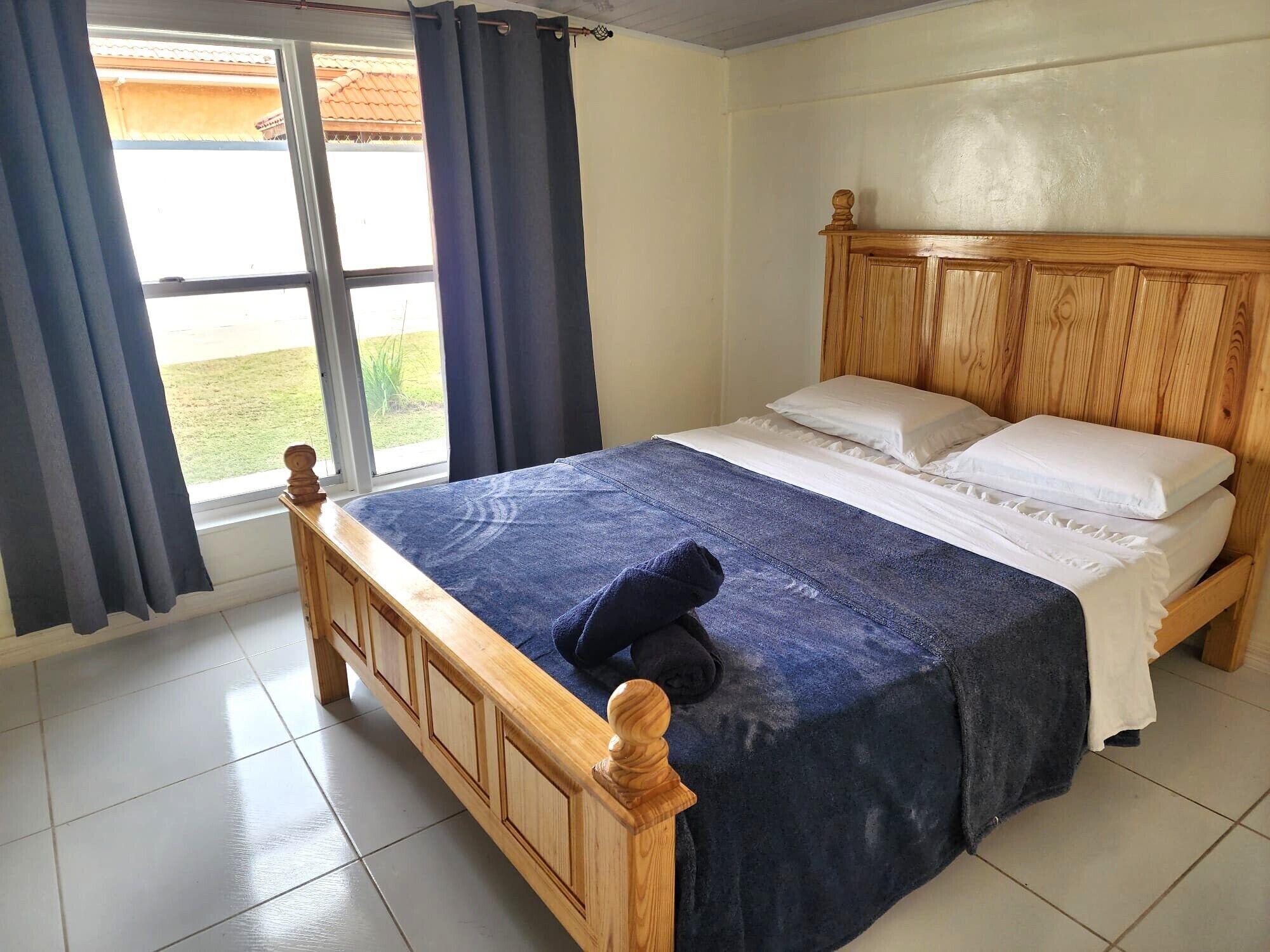 A bedroom with a wooden bed, a large window with curtains, and a view of the outdoors.