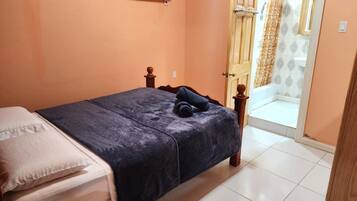A bedroom with a bed, a nightstand, a wall-mounted air conditioner, and a bathroom door.
