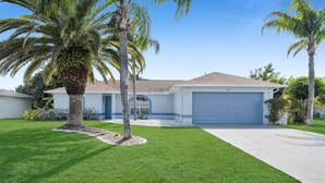 Une maison de plain-pied avec un garage, entourée d’une pelouse bien entretenue et de palmiers.