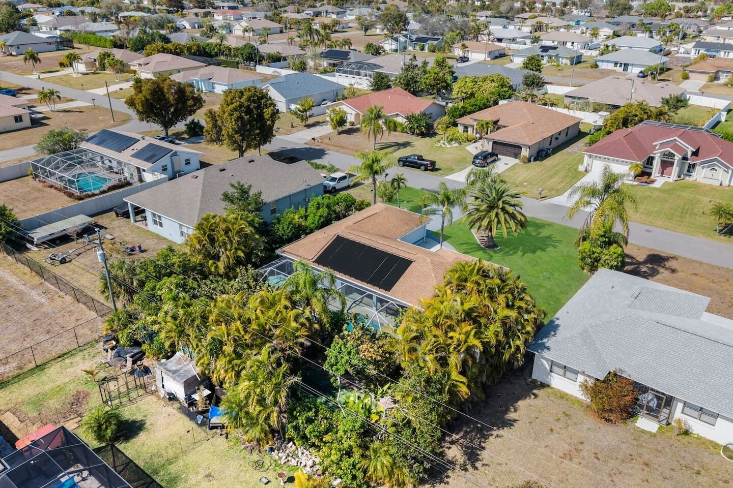 An aerial view of a residential area with houses, solar panels, and palm trees.