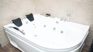 Et hvidt badekar med flere haner og en håndbruser, foran en beige væg med fliser.