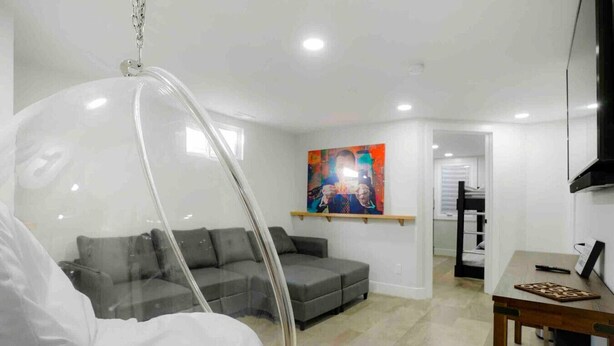 Un salon moderne avec un fauteuil suspendu, un canapé gris, un tableau au mur et une petite table sur laquelle est posé un jeu de société.