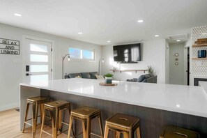 A modern kitchen with a large island, bar stools, a flat-screen TV, and a sign that reads 'RELAX AND UNWIND'.