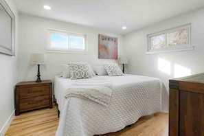 A bedroom with a bed, two bedside tables, a window, and a painting on the wall.