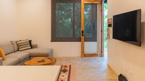 A modern living room with a sofa, a coffee table, and a TV mounted on the wall. - Casita Backdoor: Jungle Retreat, Sleeps 4-6 (Nosara)