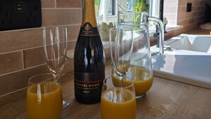 A kitchen counter with a bottle of English sparkling wine, two glasses of orange juice, and a pitcher of orange juice.