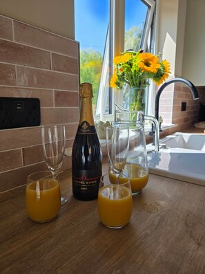 Una encimera de cocina con una botella de vino espumoso inglés, dos vasos de zumo de naranja y una jarra de zumo de naranja.