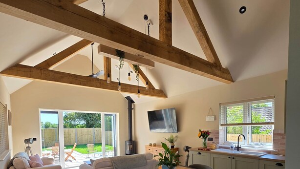 Un amplio salón con techo alto, vigas de madera a la vista, una mesa de comedor con sillas, un sofá y una zona de cocina con ventana.