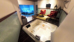 A modern bathroom with a large bathtub, a red chair, and a television mounted on the wall. - Pousada Liberte-se in Búzios  (Buzios)