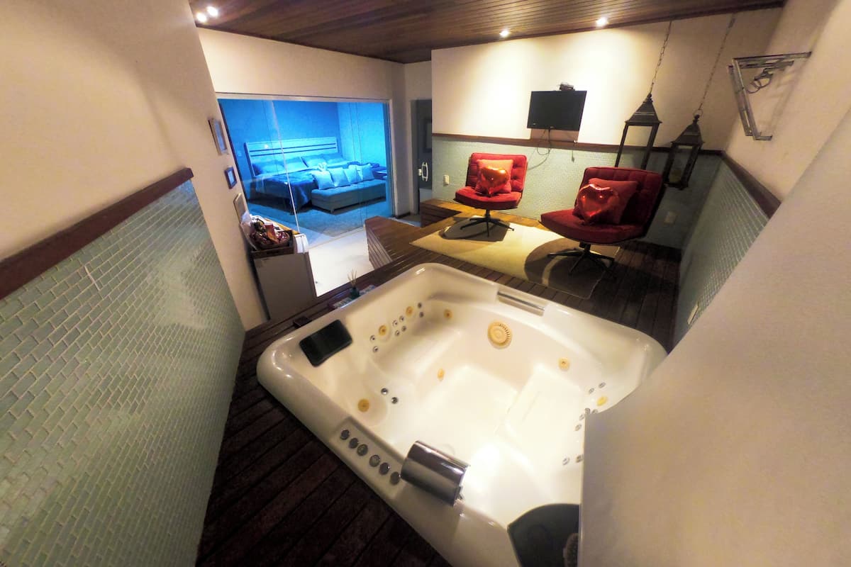A modern bathroom with a large bathtub, a red chair, and a television mounted on the wall.