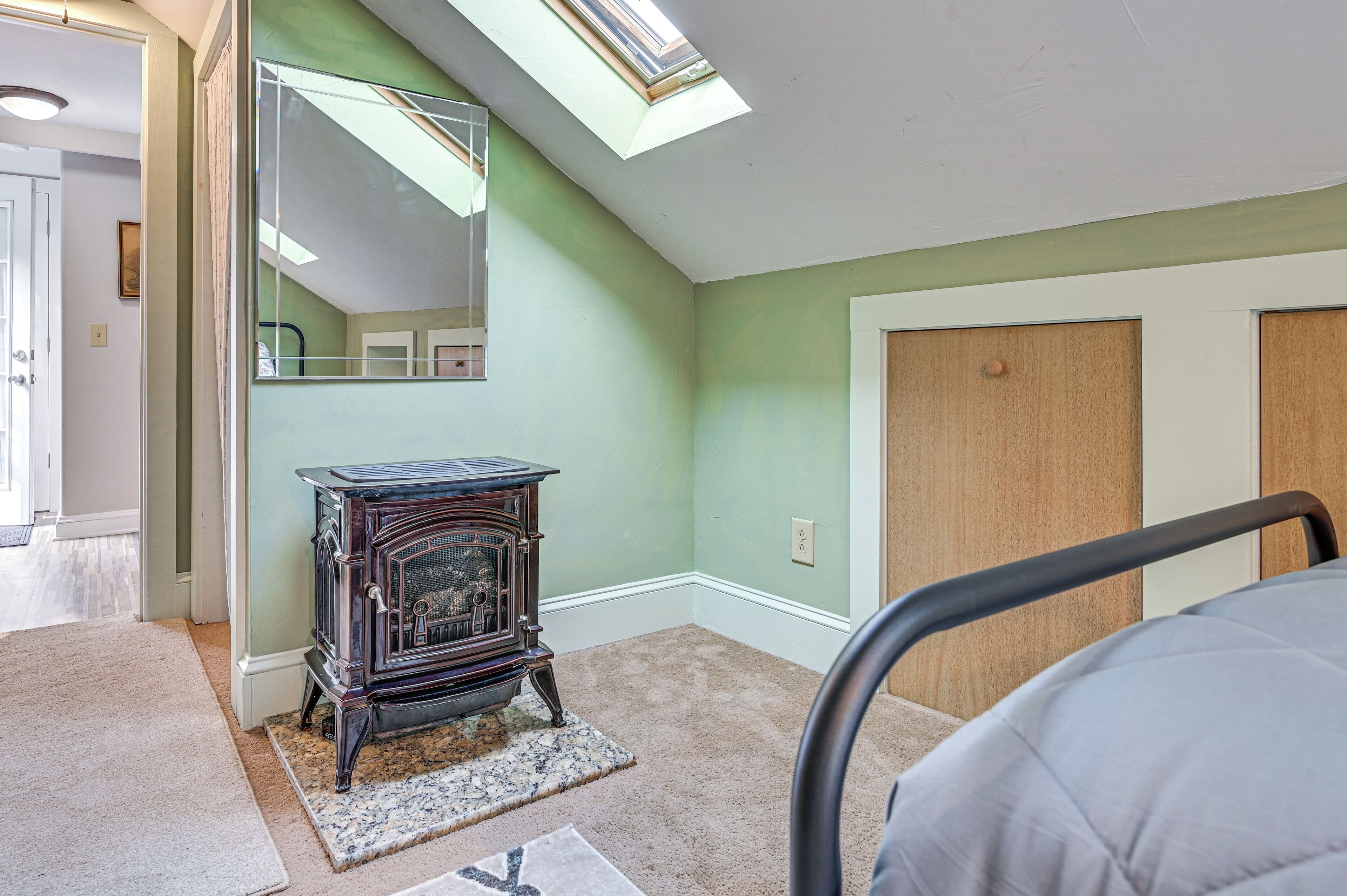 A room with a skylight, a vintage stove, a bed, and a door.