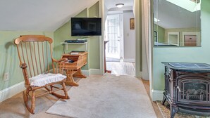 A room with a wooden rocking chair, a television mounted on the wall, and a vintage stove. - Quaint & Charming Cherry Valley Escape! (Cherry Valley)