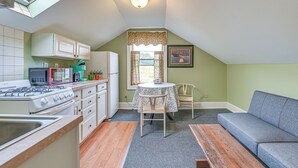 A compact kitchen with a gas stove, microwave, and refrigerator. There is a dining table with chairs and a grey sofa in the adjacent living area. - Quaint & Charming Cherry Valley Escape! (Cherry Valley)