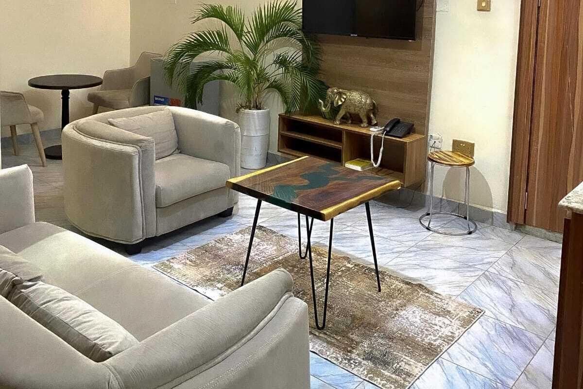 A living room with a sofa, armchairs, a coffee table, a TV mounted on the wall, a potted plant, and a wooden cabinet.