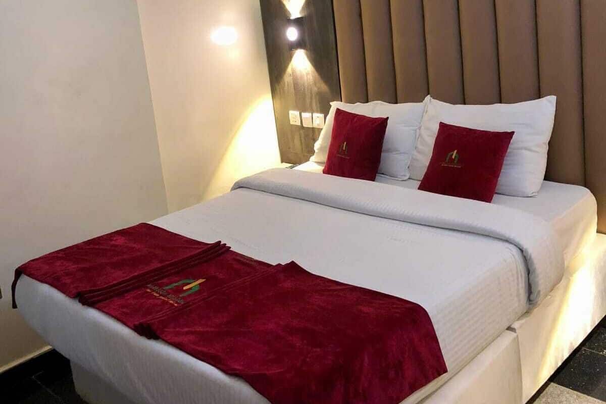 A hotel room with a large bed, a red throw blanket, and a headboard with vertical slats.