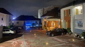 A nighttime street view with buildings, parked cars, and a lit entrance to a property. - Marrisson residence (Abuja)