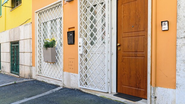 Un edificio con puerta de madera, ventana con celosía y maceta con flores.