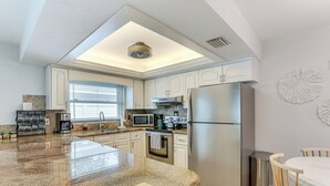 Een moderne keuken met een centraal eiland, roestvrijstalen apparatuur en een eethoek met een houten tafel en stoelen.