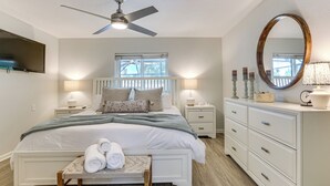 Een slaapkamer met een bed, nachtkastjes, een kaptafel, een spiegel en een plafondventilator.