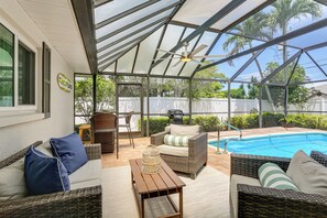 Ein überdachter Außenbereich mit Korbmöbeln, einem Pool und einem Deckenventilator.