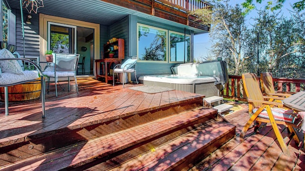 A deck with outdoor furniture, a hot tub, and a wooden staircase leading to a door. - Hot Tub & Mtn Views: Charming Utah Canyon Retreat (Sandy)