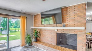 A modern living room with a brick fireplace, a flat-screen TV mounted above it, and a sliding glass door leading to a patio. - 4 Mi to Loris Nature Park: Family Home w/ Yard (Loris)