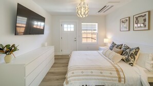 Un dormitorio con una cama grande, un televisor de pantalla plana en la pared, una mesita de noche con lámpara y una planta en maceta.