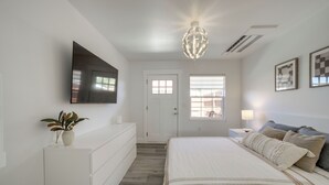 Ein Schlafzimmer mit einem Bett, einem an der Wand montierten Fernseher, einer Deckenleuchte und einer Tür mit Fenstern.