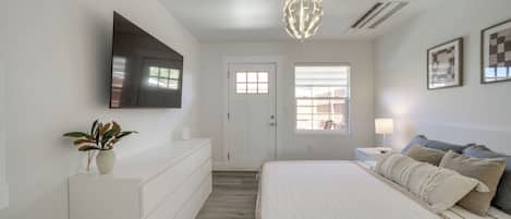 A bedroom with a bed, a TV mounted on the wall, a ceiling light fixture, and a door with windows.