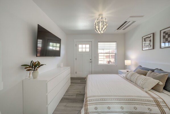 Quarto com cama, televisão fixada na parede, luminária no teto e porta com janelas.