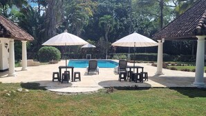 Zona de piscina con techo de baldosas, mobiliario exterior y una piscina.