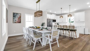 A modern kitchen with white cabinets, stainless steel appliances, and a dining area with white chairs and a wooden table. - 4BR beach club w/ Hot tub + Pool + Game room (North Myrtle Beach)
