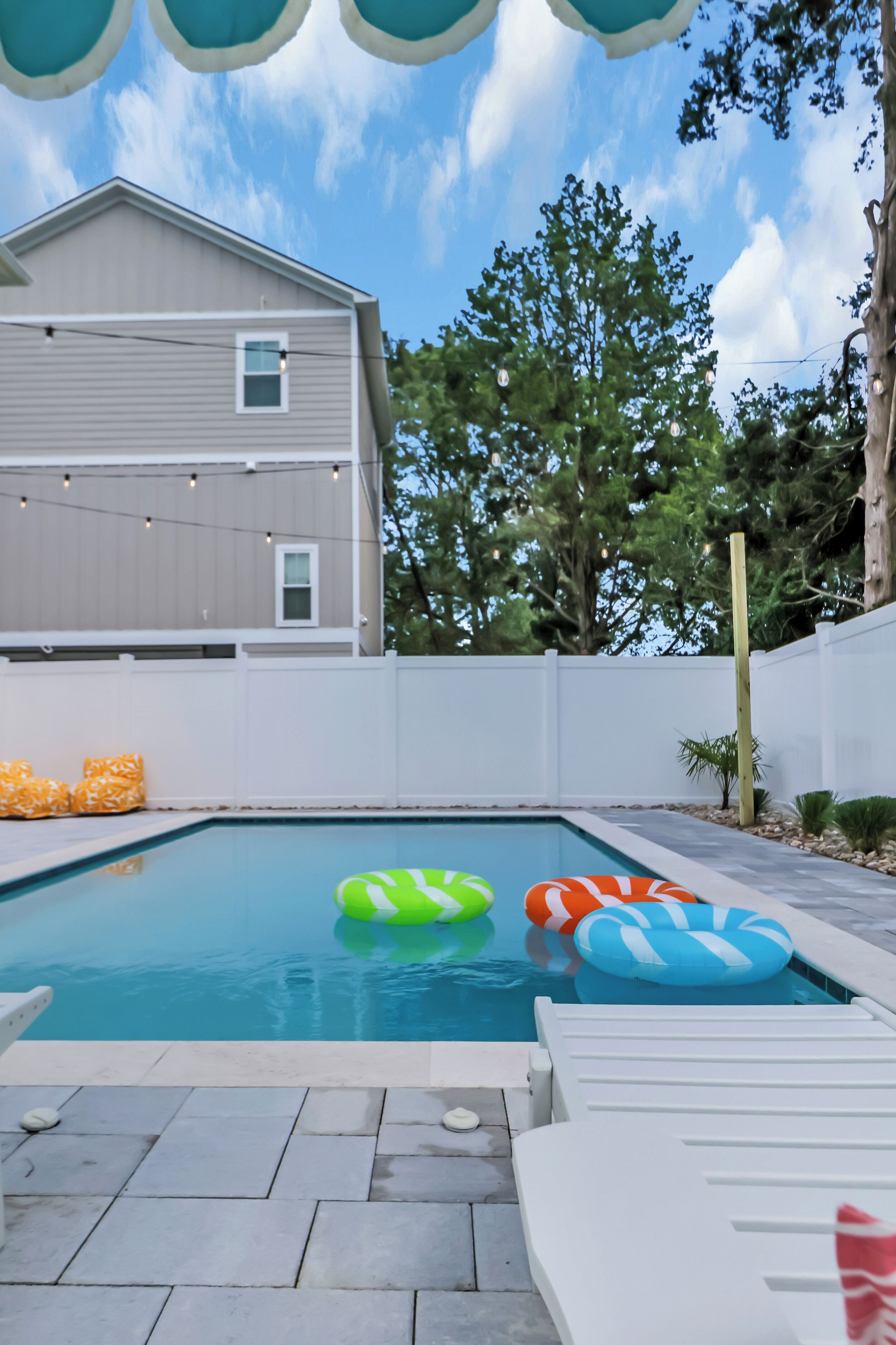 A swimming pool with inflatable rings, a white fence, and a house in the background.