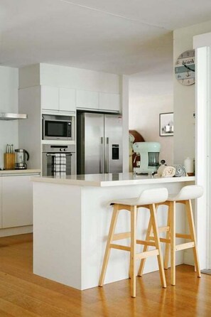 Una cocina moderna con armarios blancos, una isla central con taburetes, microondas, horno y refrigerador.