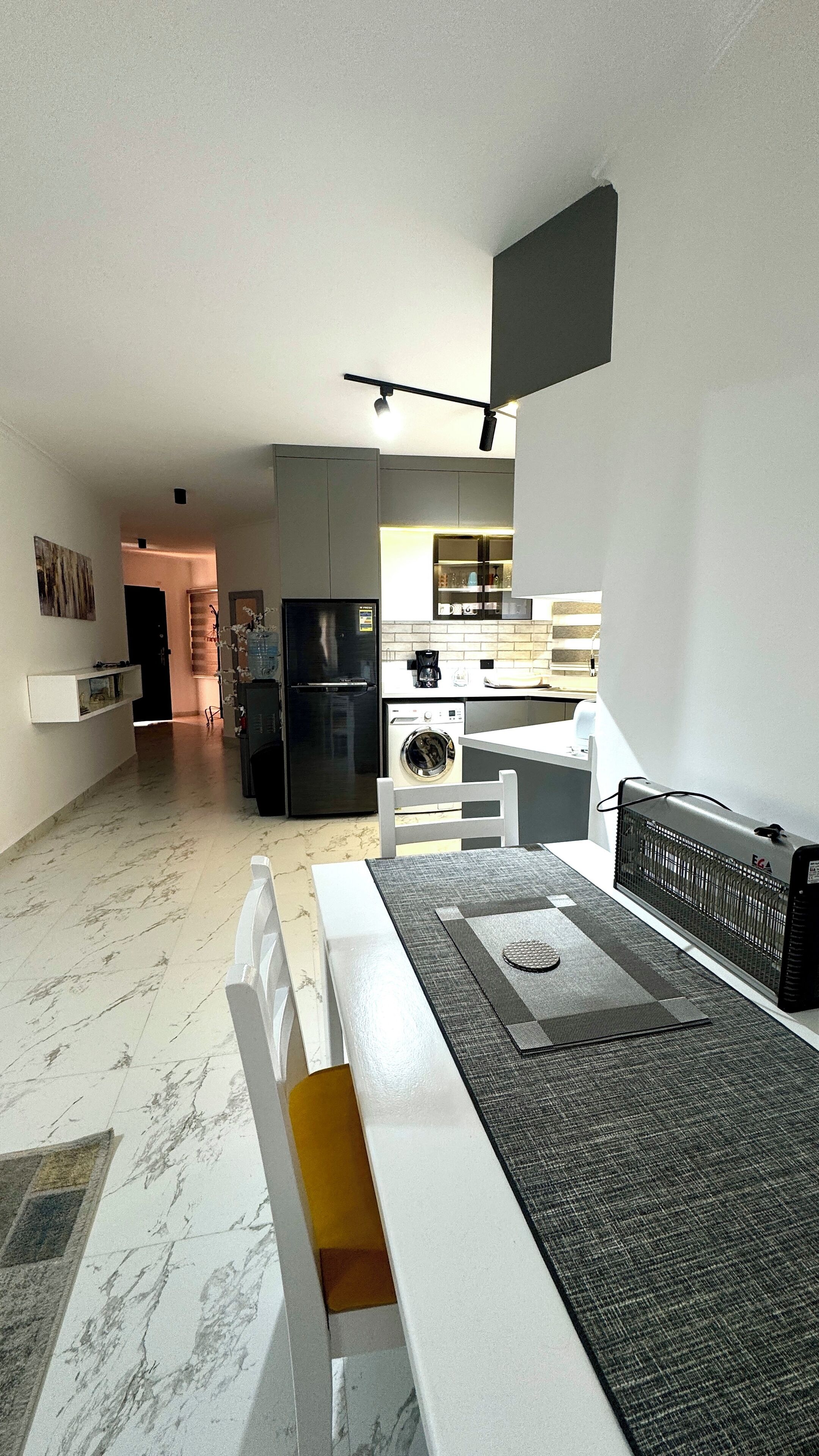 Eine moderne Küche mit Einbauofen, Kühlschrank und Waschmaschine. Ein Essbereich mit Tisch und Stühlen ist ebenfalls vorhanden.