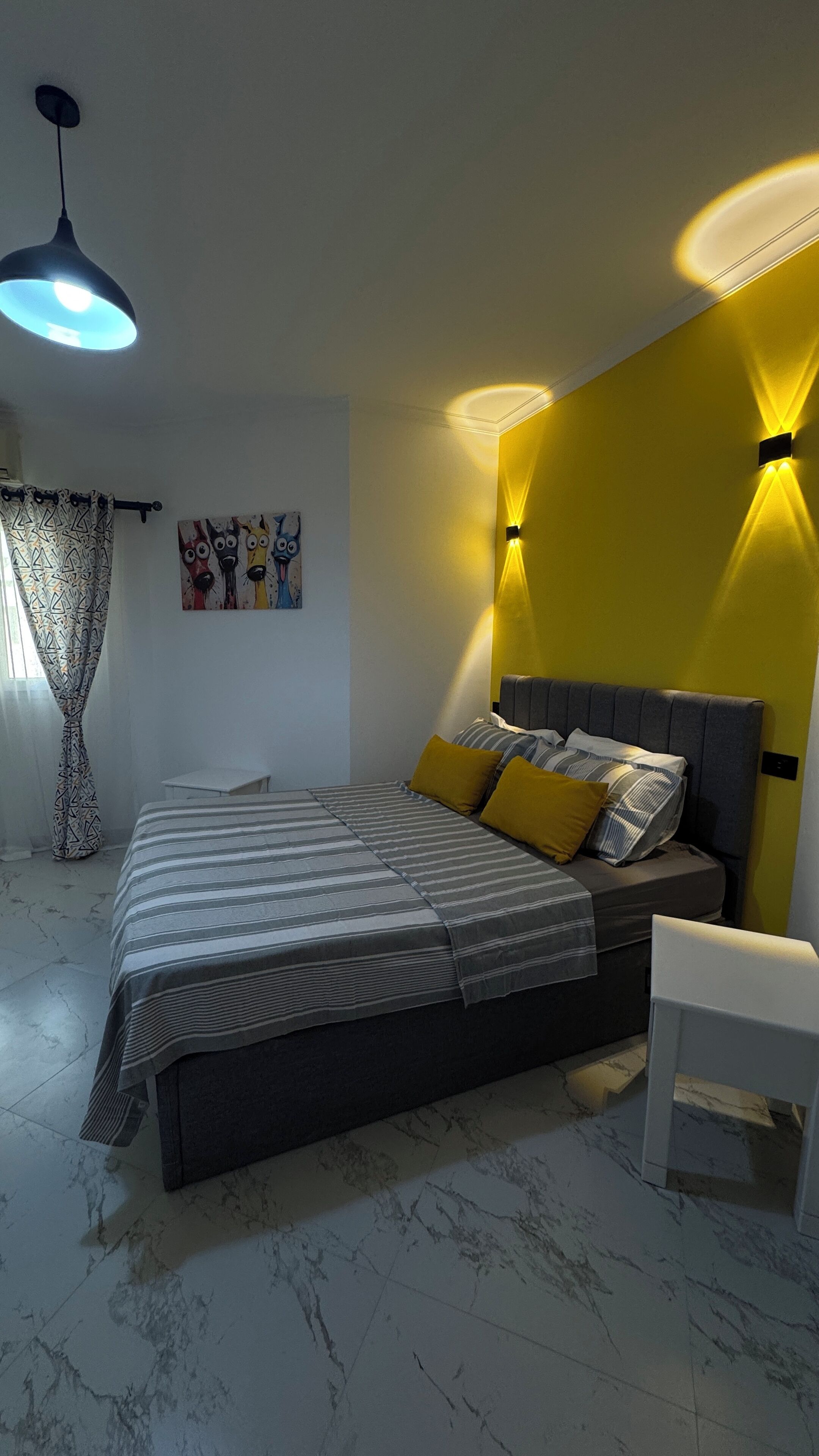 Un dormitorio moderno con cama, mesita de noche, silla, un cuadro y una lámpara de techo.