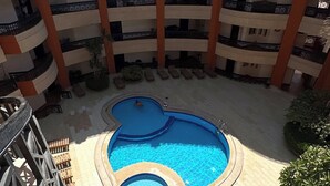 A multi-story building with a central courtyard featuring a swimming pool. - Modern 2-Bedroom flat in prime compound with pool & all  Amenities (Red Sea Governorate)