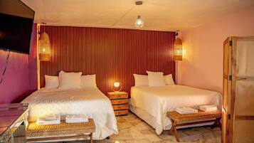 A hotel room with two beds, a television, a wooden wardrobe, and a woven bench.