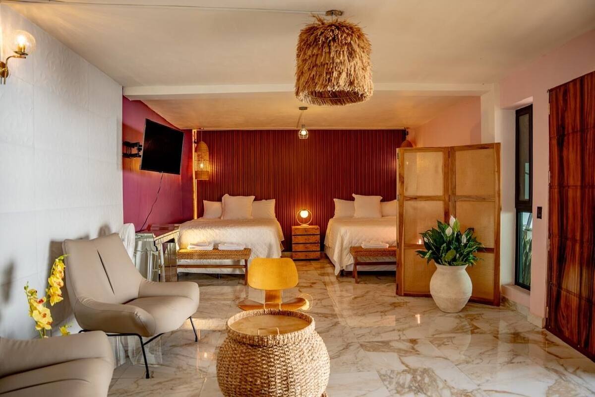 A hotel room with a bed, two bedside tables, a chair, a lamp, a plant, and a television.