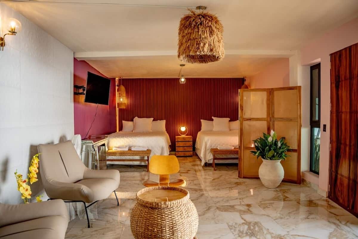 Une chambre dâhĂŽtel comprenant un lit, deux tables de chevet, une chaise, une lampe, une plante et un tĂ©lĂ©viseur.
