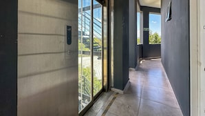 A modern hallway with large glass doors leading to a balcony, a Samsung charging station, and an emergency exit sign.