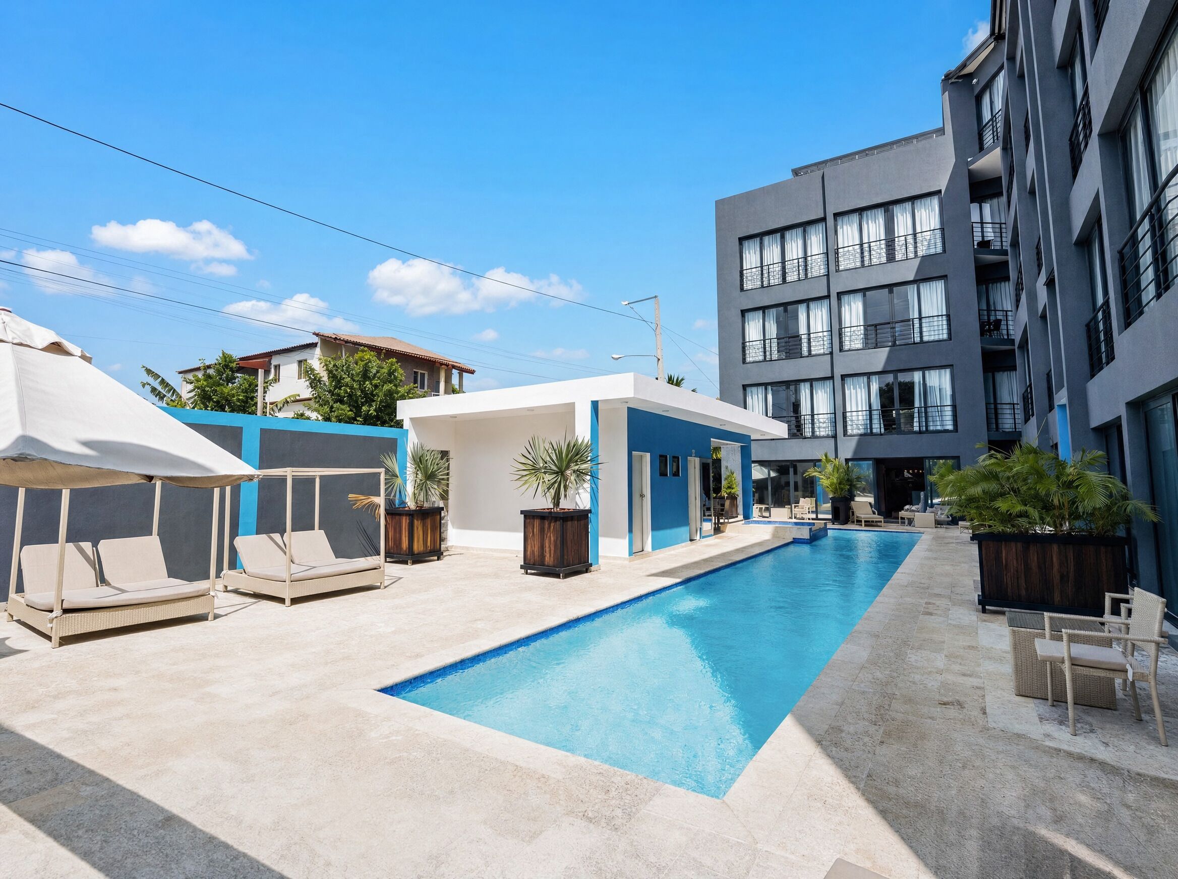 A swimming pool area with lounge chairs, a covered seating area, and a modern building with balconies.