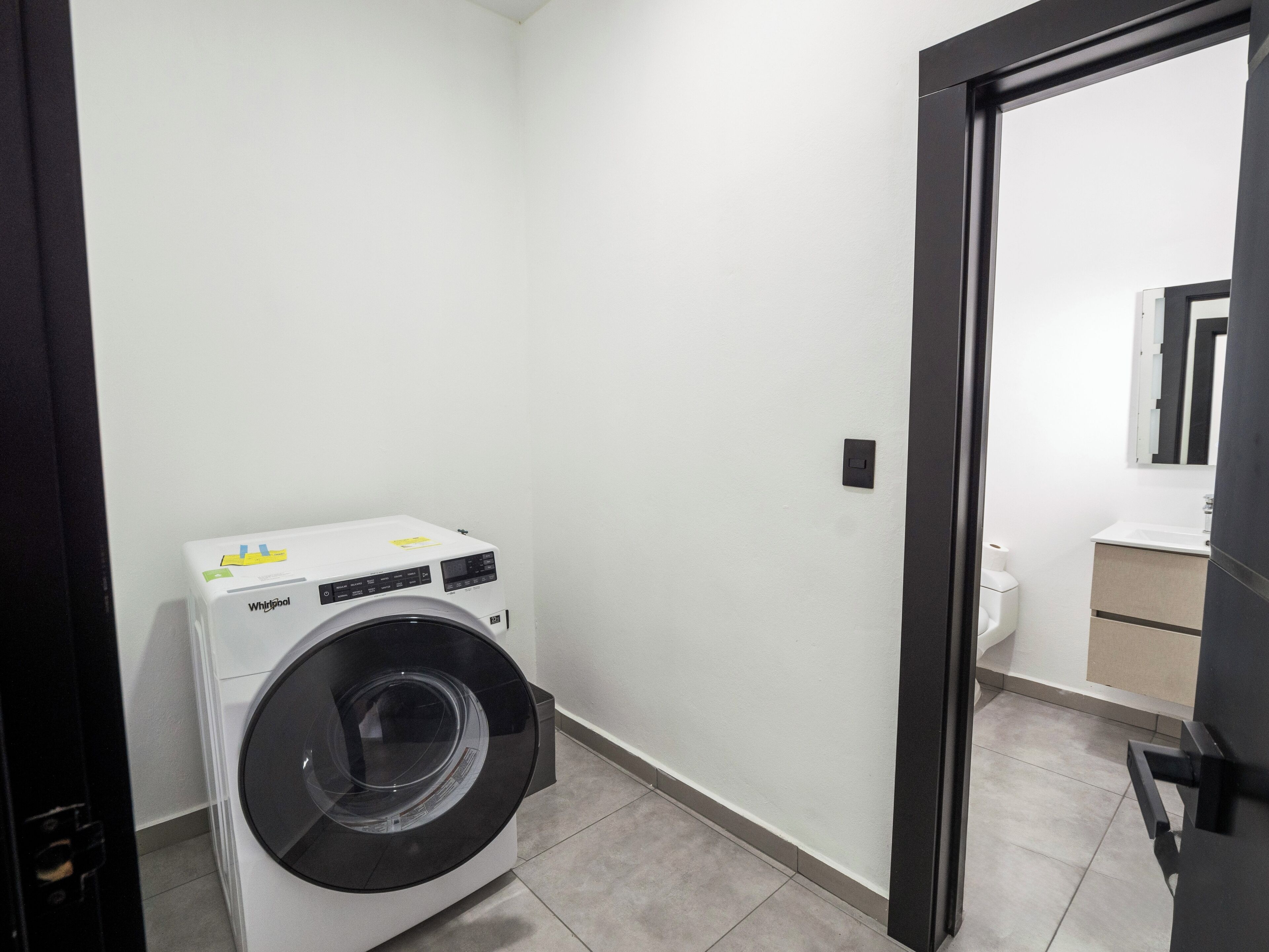 A compact laundry room with a front-loading washer and dryer, a small sink, and a mirror above the sink.