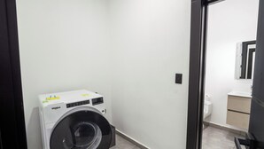 A compact laundry room with a front-loading washer and dryer, a small sink, and a mirror above the sink.