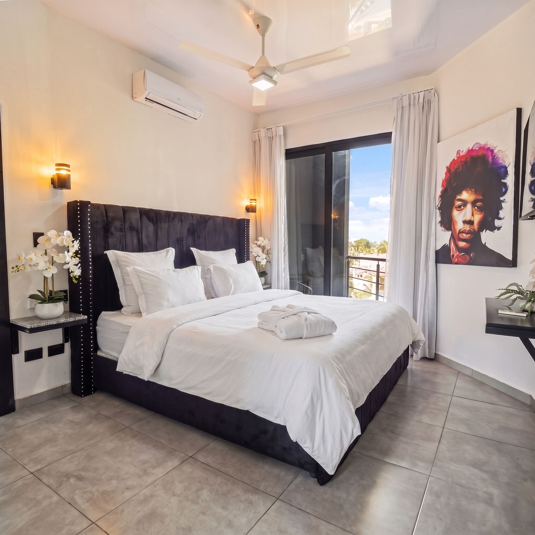 Une chambre d’hôtel avec un grand lit, un ventilateur de plafond, un appareil de climatisation et un balcon avec vue.