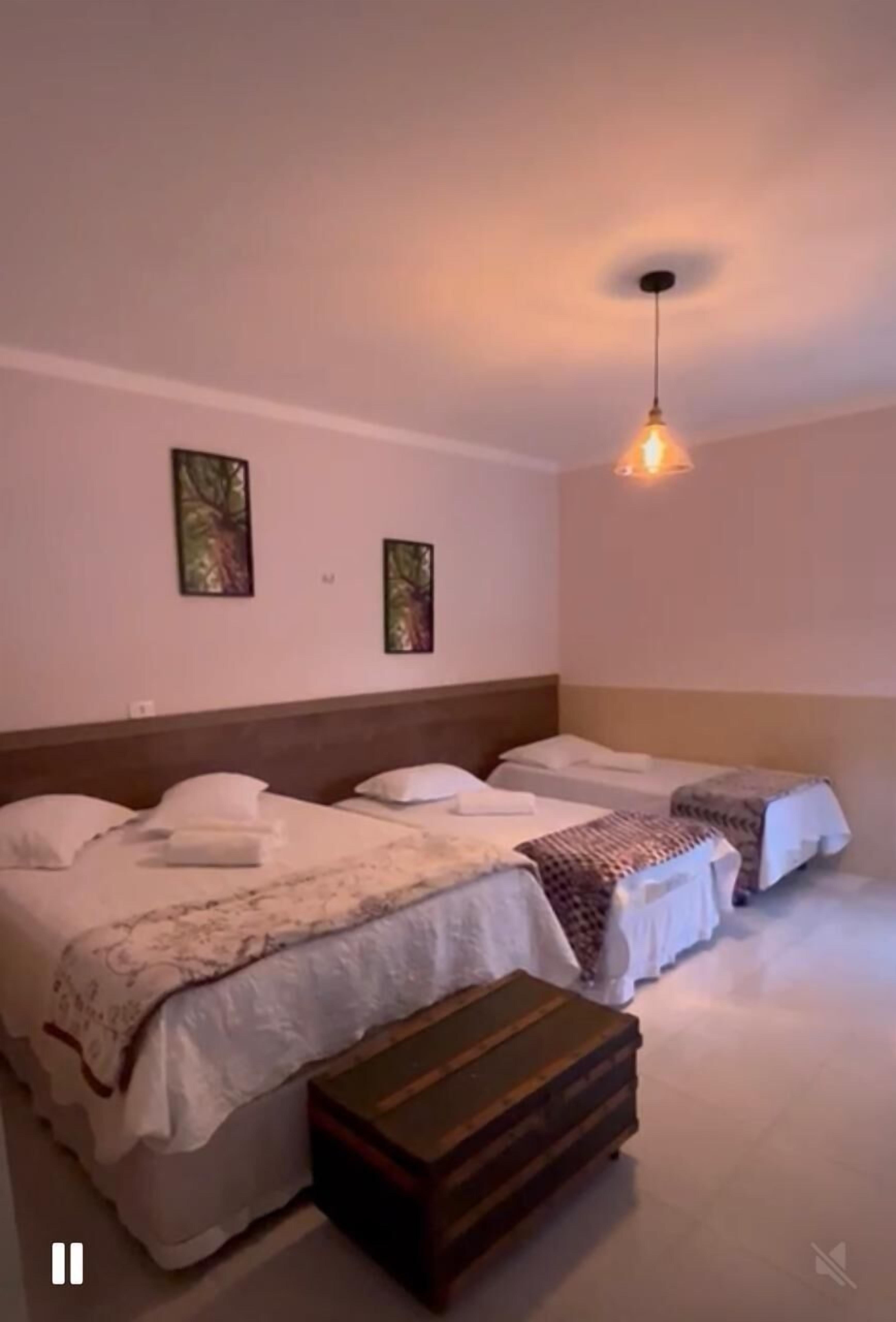 Quarto de hotel com duas camas de solteiro, um banco de madeira e um lustre.