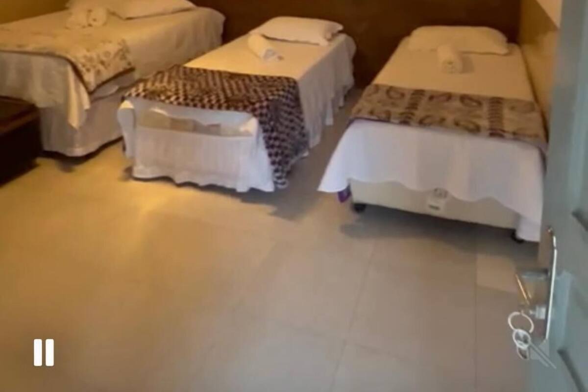 A hotel room with three single beds, a ceiling light, and two wall-mounted paintings.
